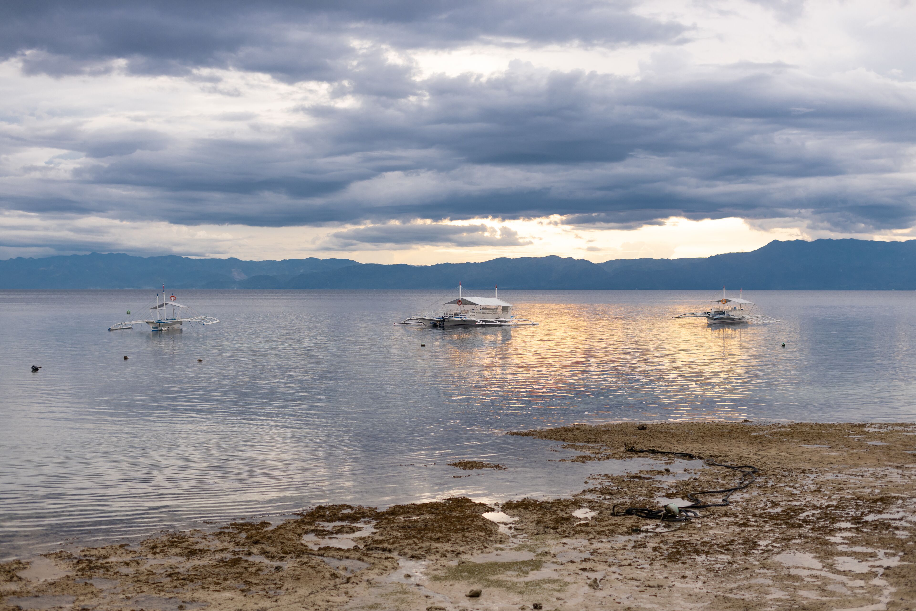 A calm lake with boats and distant mountains under a cloudy sky.