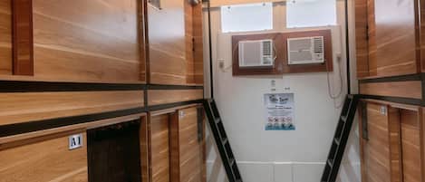 Ein holzgetäfeltes Zimmer im Blockhausstil mit Holzboden, einem Fenster mit Jalousien, einer Wand-Klimaanlage und einem Poster an der Wand.