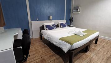 A hotel room with a bed, bedside table, desk, chair, and a fan.