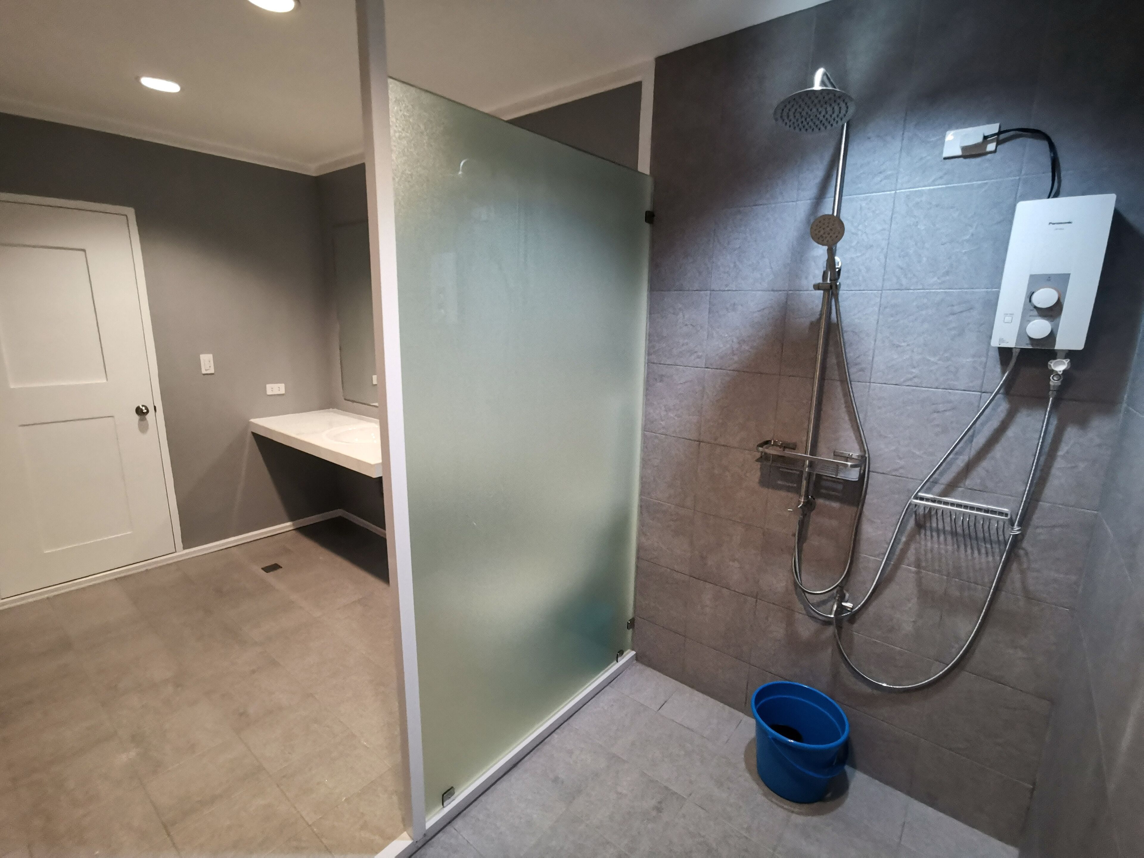 A modern bathroom with a glass shower enclosure, a built-in sink, and a blue bucket.