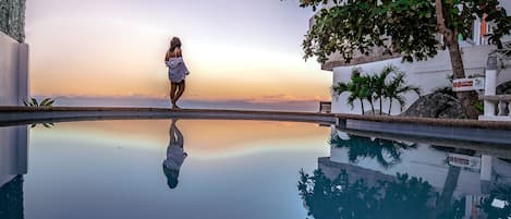 A woman standing by a pool with a sunset view.