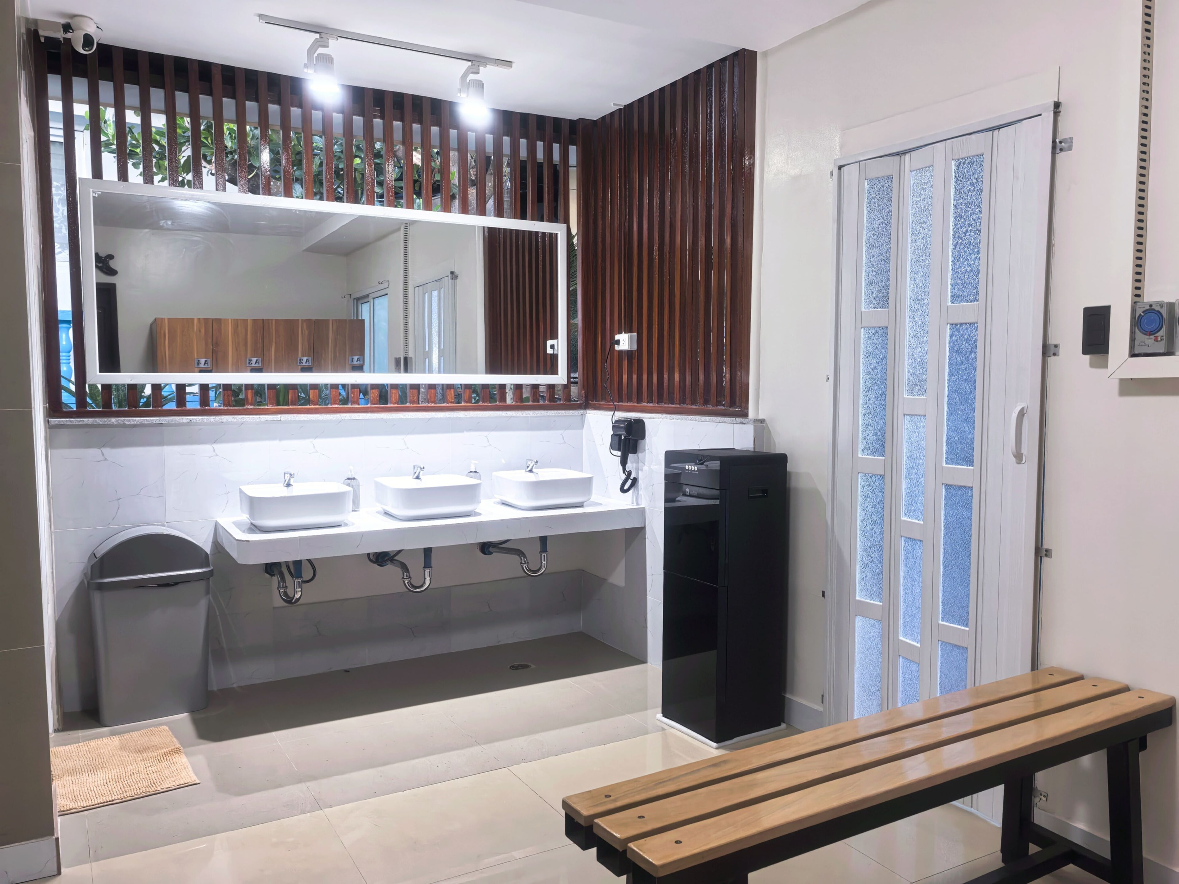 A modern bathroom with three sinks, a toilet, and a bench.