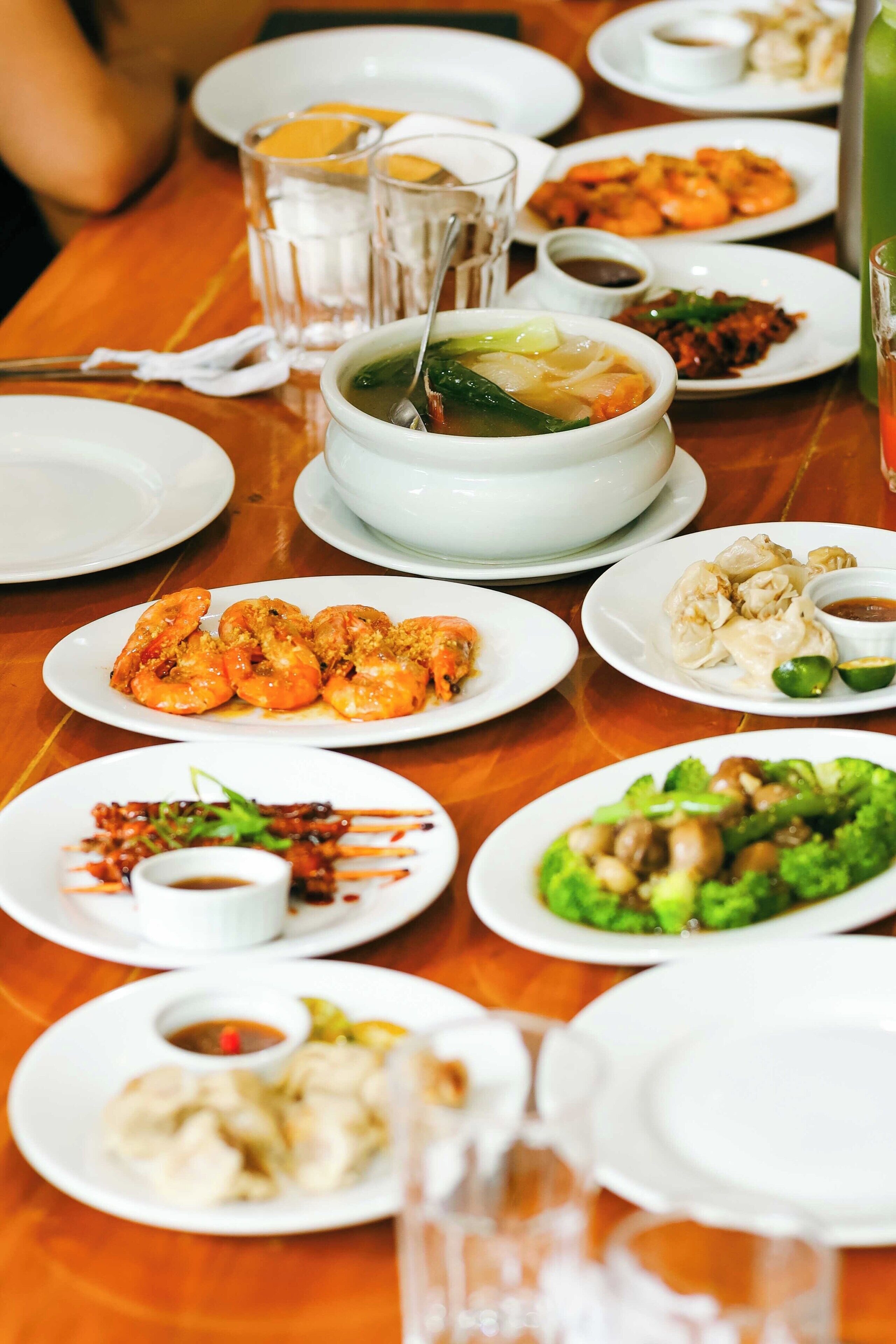 A dining table with various dishes, including shrimp, dumplings, and vegetables, along with glasses of water and tea.