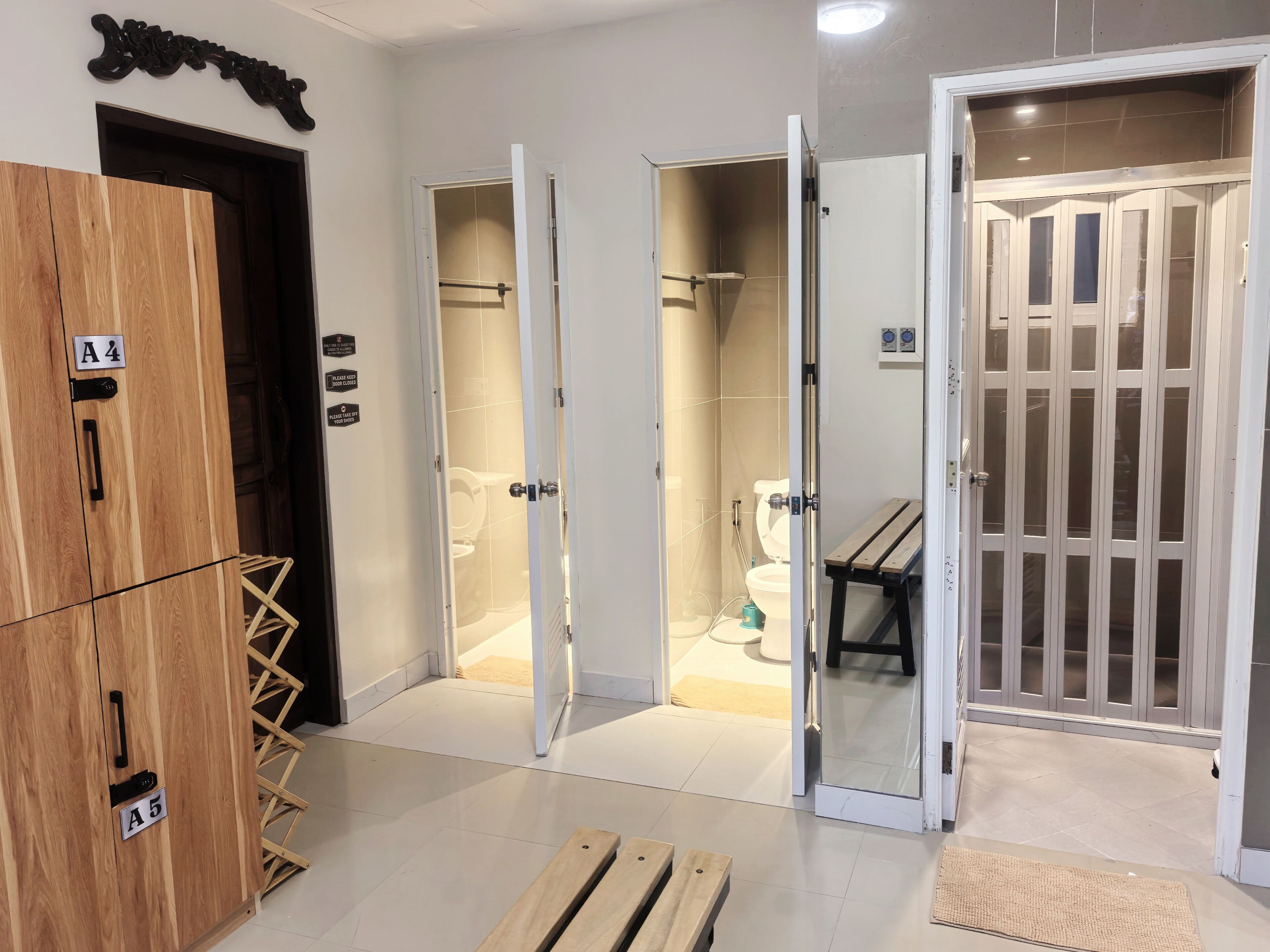 A hotel room with a wooden wardrobe, a shower area, and a glass door leading to a bathroom.