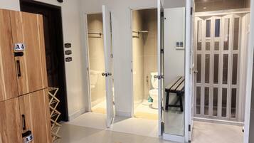 A hotel room with a wooden wardrobe, a shower area, and a glass door leading to a bathroom.