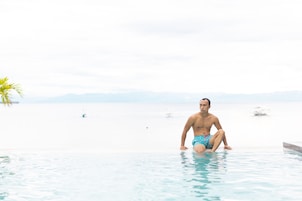 A man sitting in a pool with a view of the sea and boats in the background.