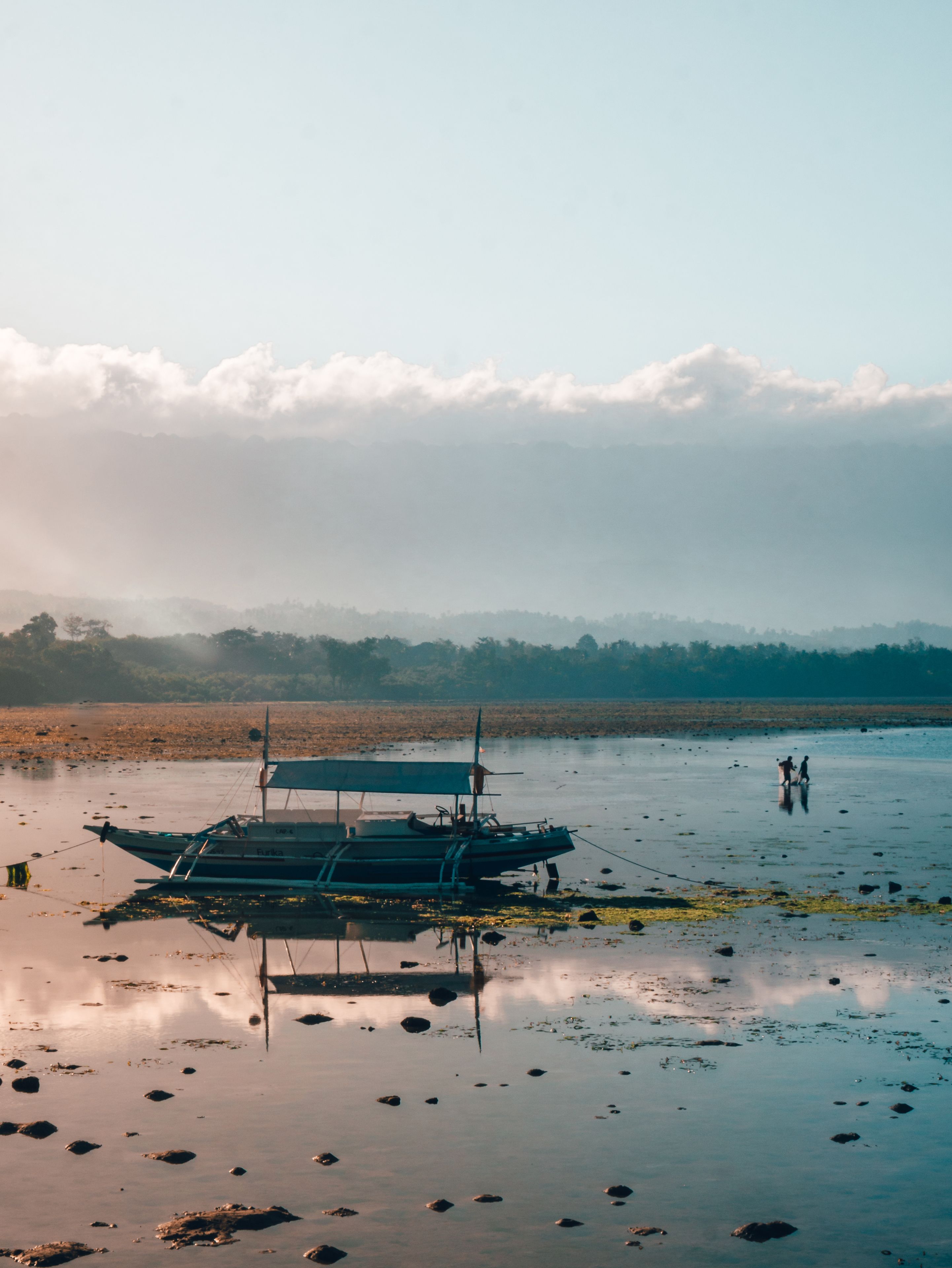 A boat on a calm water body with a forested background and a cloudy sky.