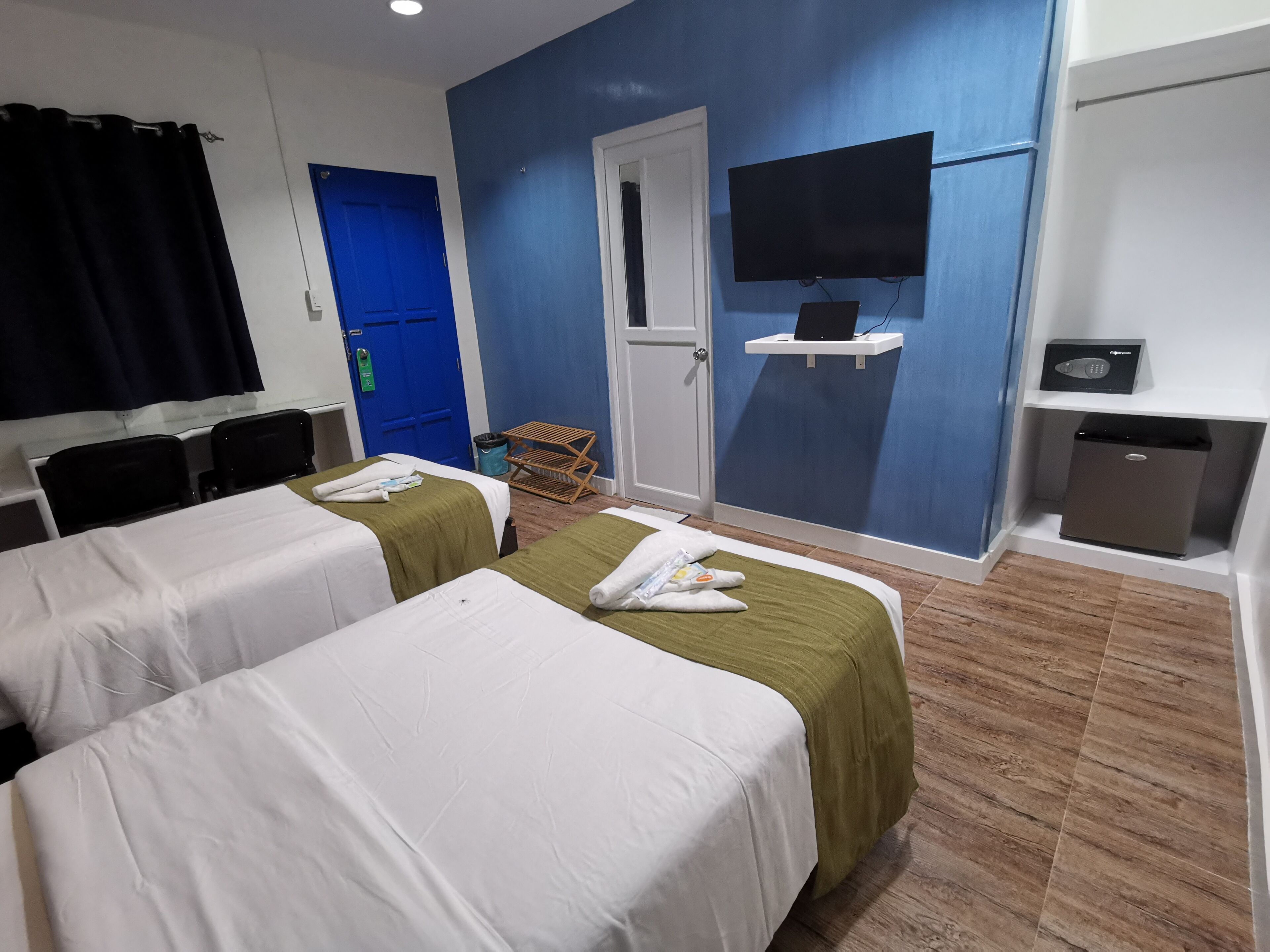 Ein Hotelzimmer mit zwei Betten, einem Fernseher, einer Minibar und einer blauen Tür.