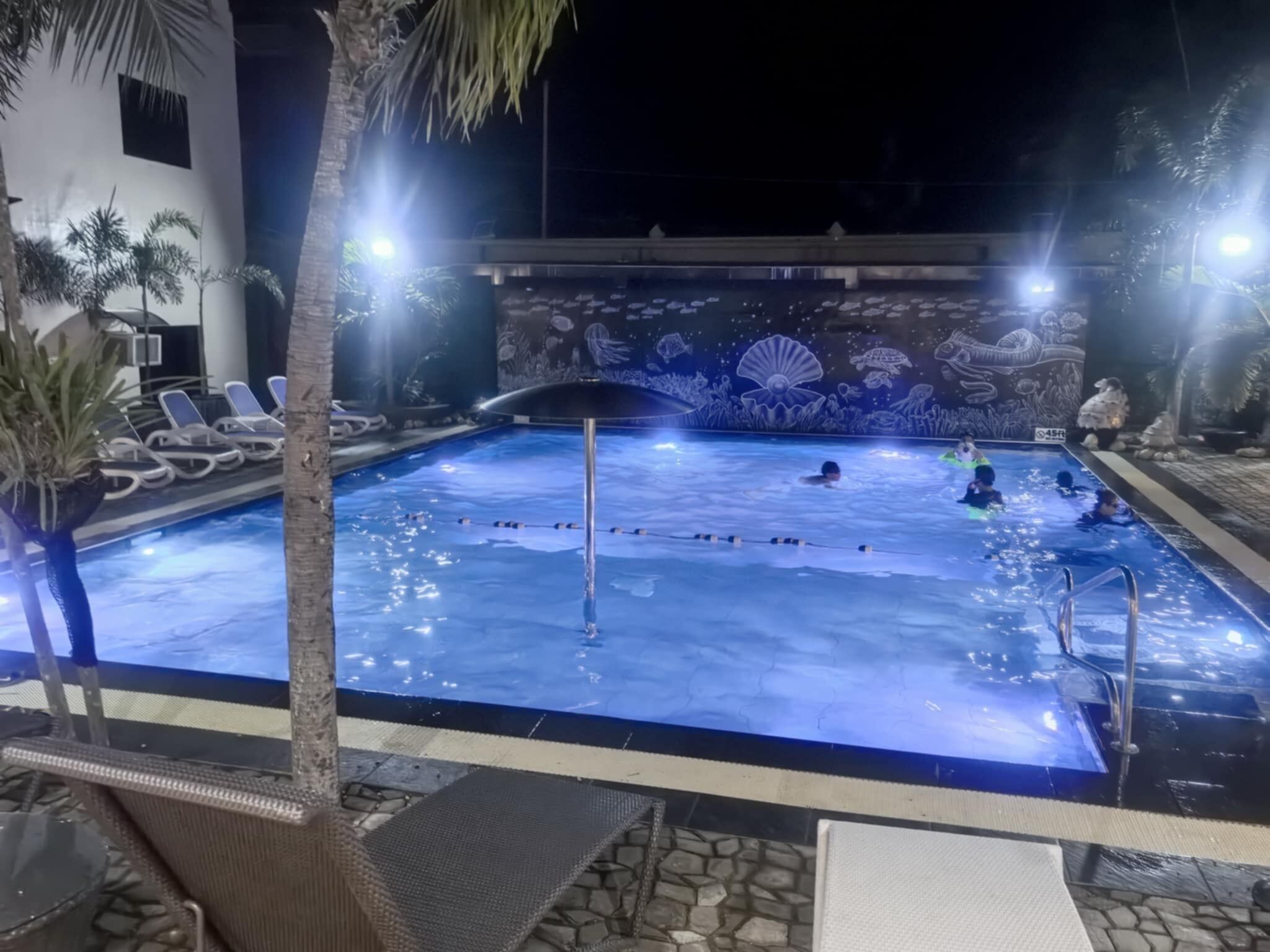 Una piscina con murales subacuáticos, sillas de descanso y palmeras.