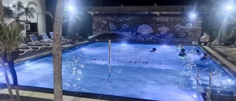 Una piscina con murales subacuáticos, sillas de descanso y palmeras.