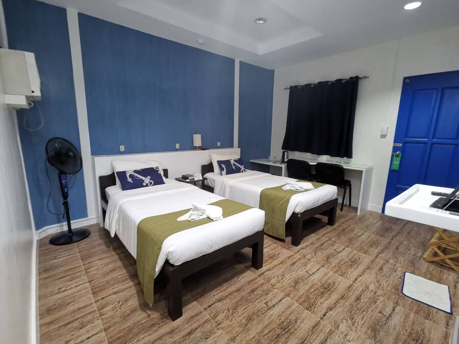 Habitación de hotel con dos camas, un escritorio, una silla, un ventilador y una puerta azul.