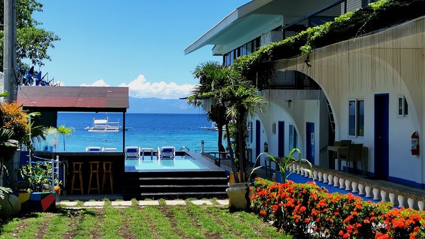 Zona de piscina con vista al océano, un espacio de estar cubierto y un edificio con puertas azules.