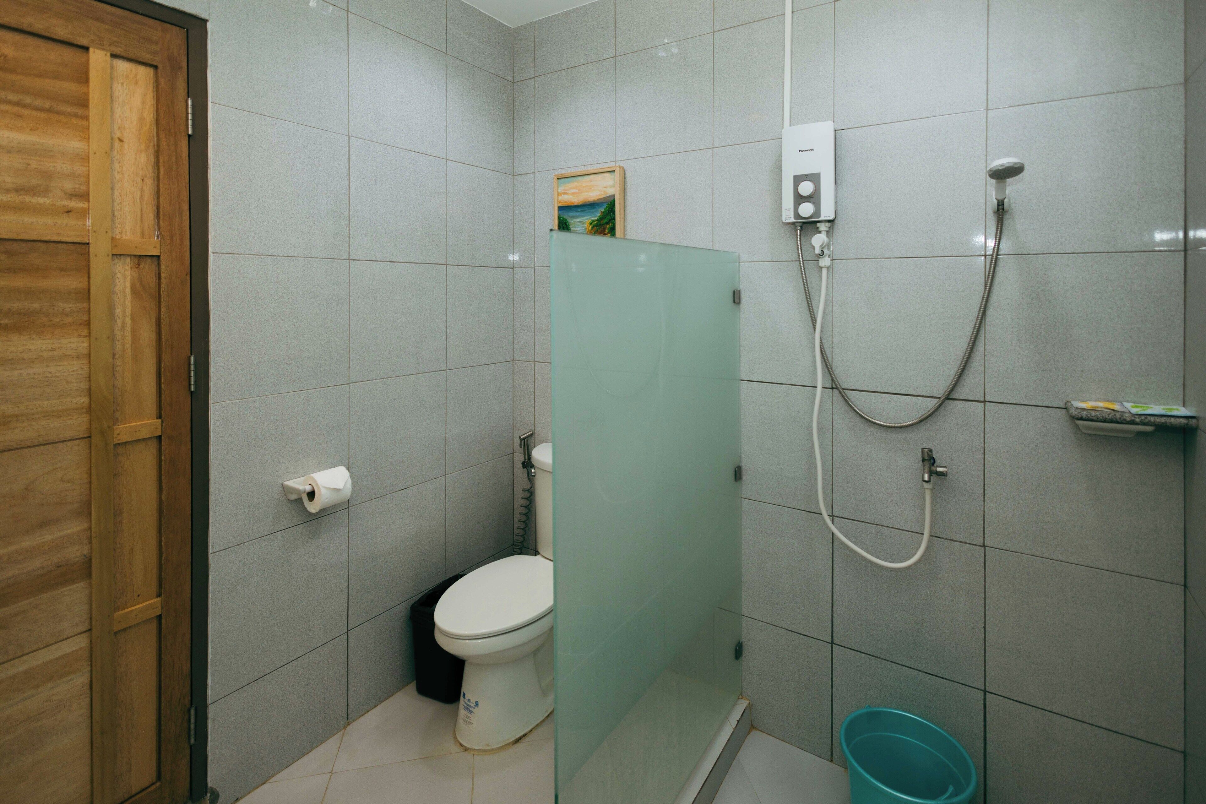 Een kleine badkamer met toilet, een douchecabine van glas en een emmer.