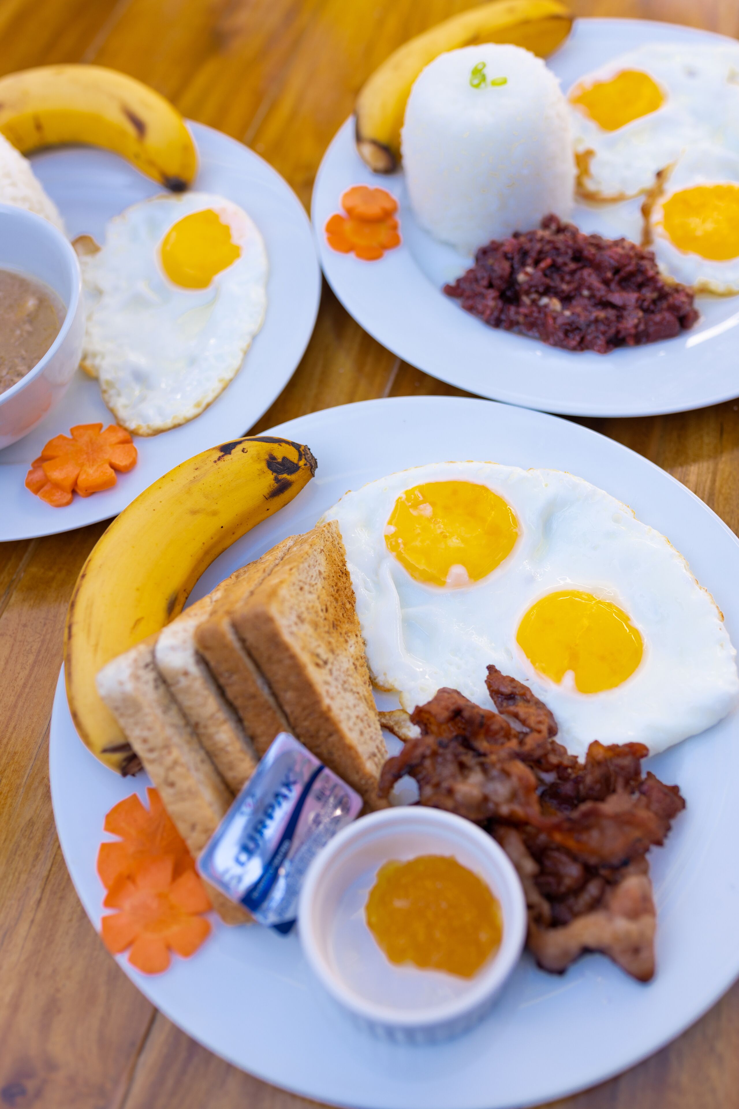 Une assiette de petit-déjeuner comprenant des œufs, du bacon, des toasts, une banane et un petit bol de sauce.