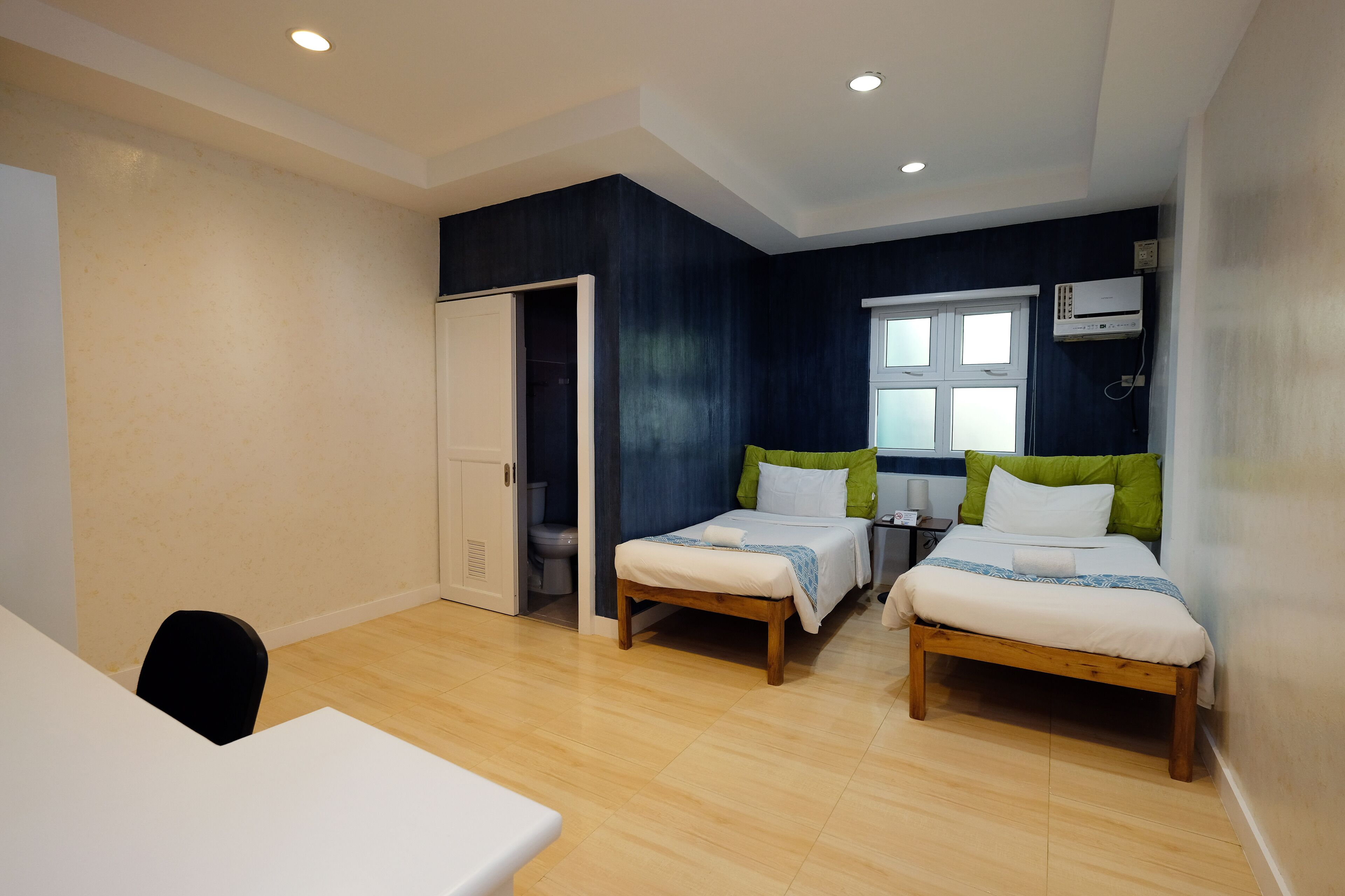A bedroom with two single beds, a wooden floor, a white table, and a door leading to a bathroom.