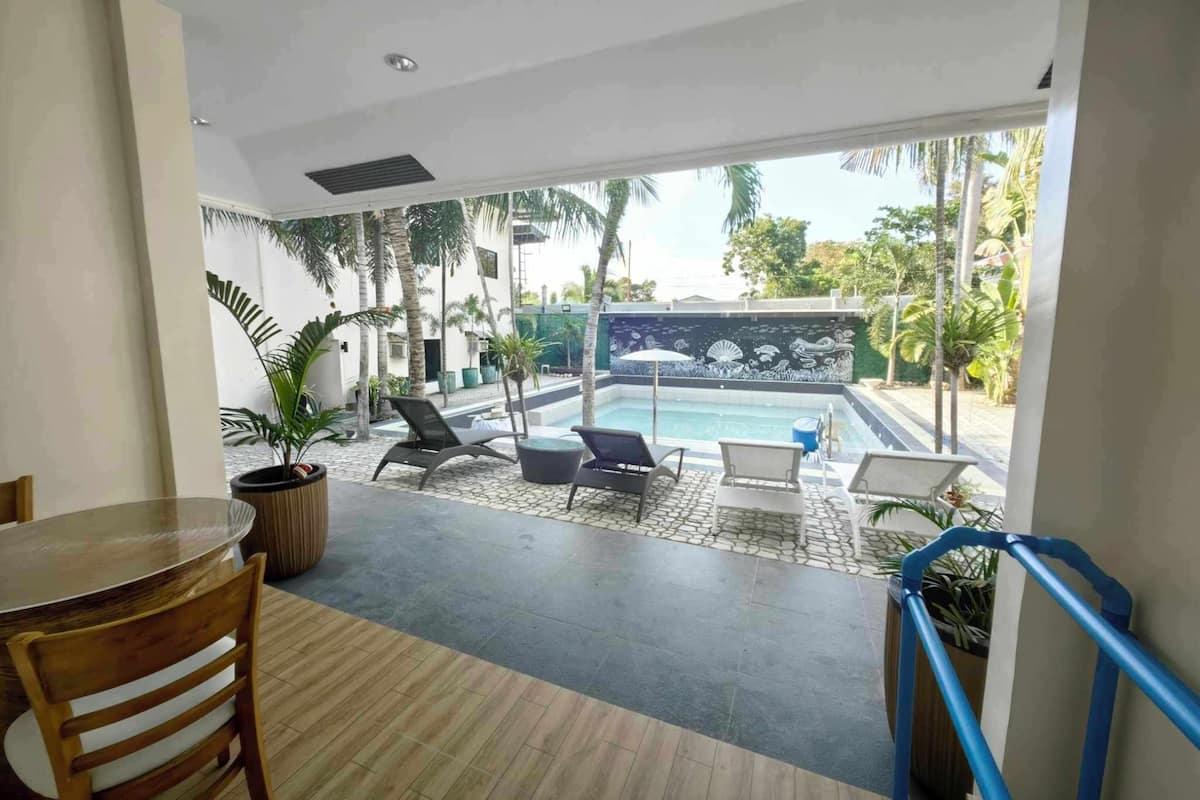 A modern hotel room with a pool, outdoor seating, and a view of palm trees.