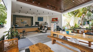 Amplio espacio interior con techo de madera, mostrador de recepción, arreglos de asientos y plantas en macetas.