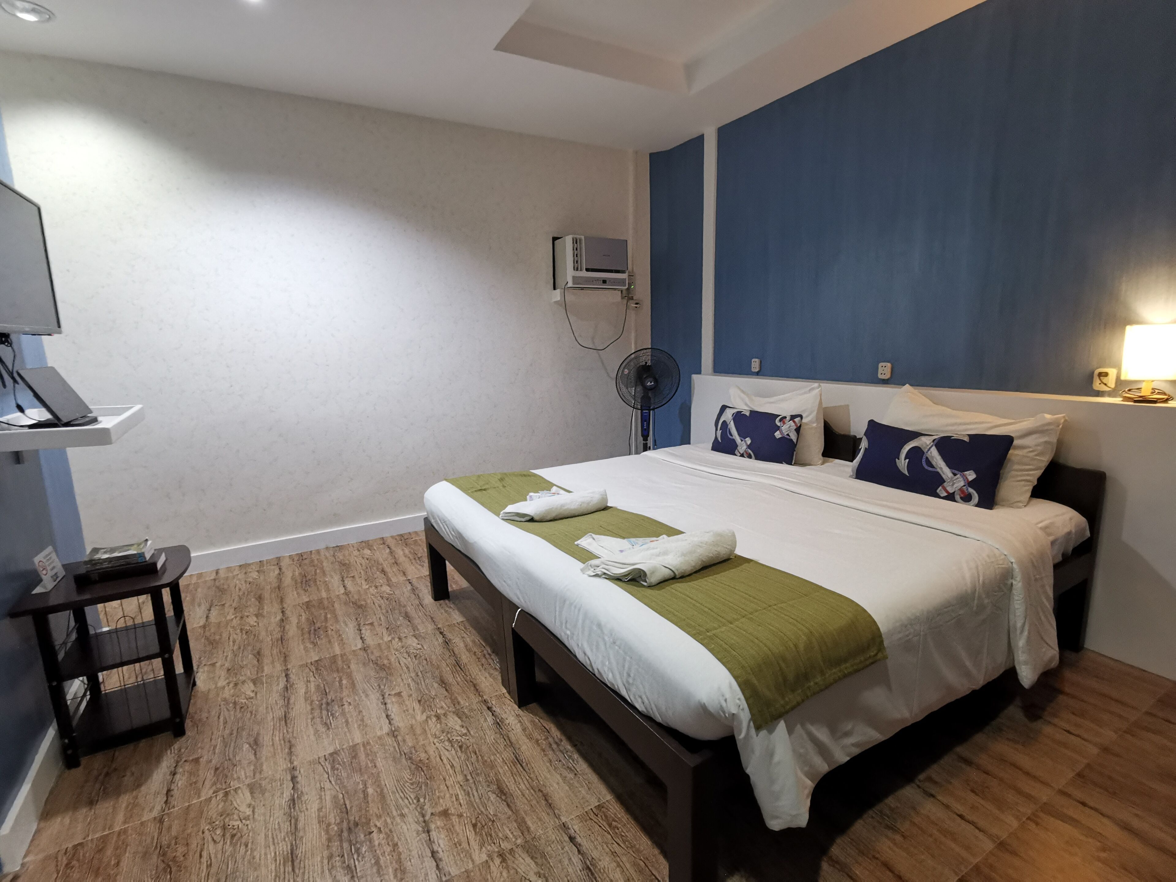 A hotel room with a bed, a desk, a fan, and a wall-mounted air conditioner.