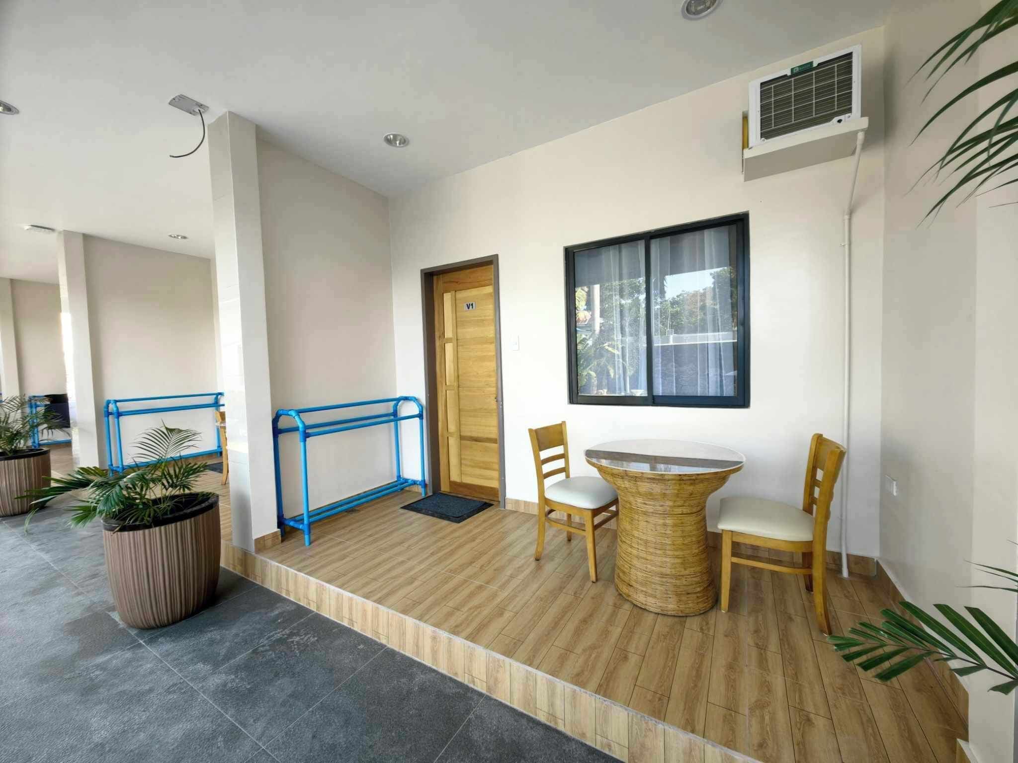 A modern interior with a wooden floor, a small round table with chairs, a blue metal bench, and potted plants.