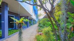 Un sendero bordeado de abundante vegetación y un edificio moderno con detalles azules.