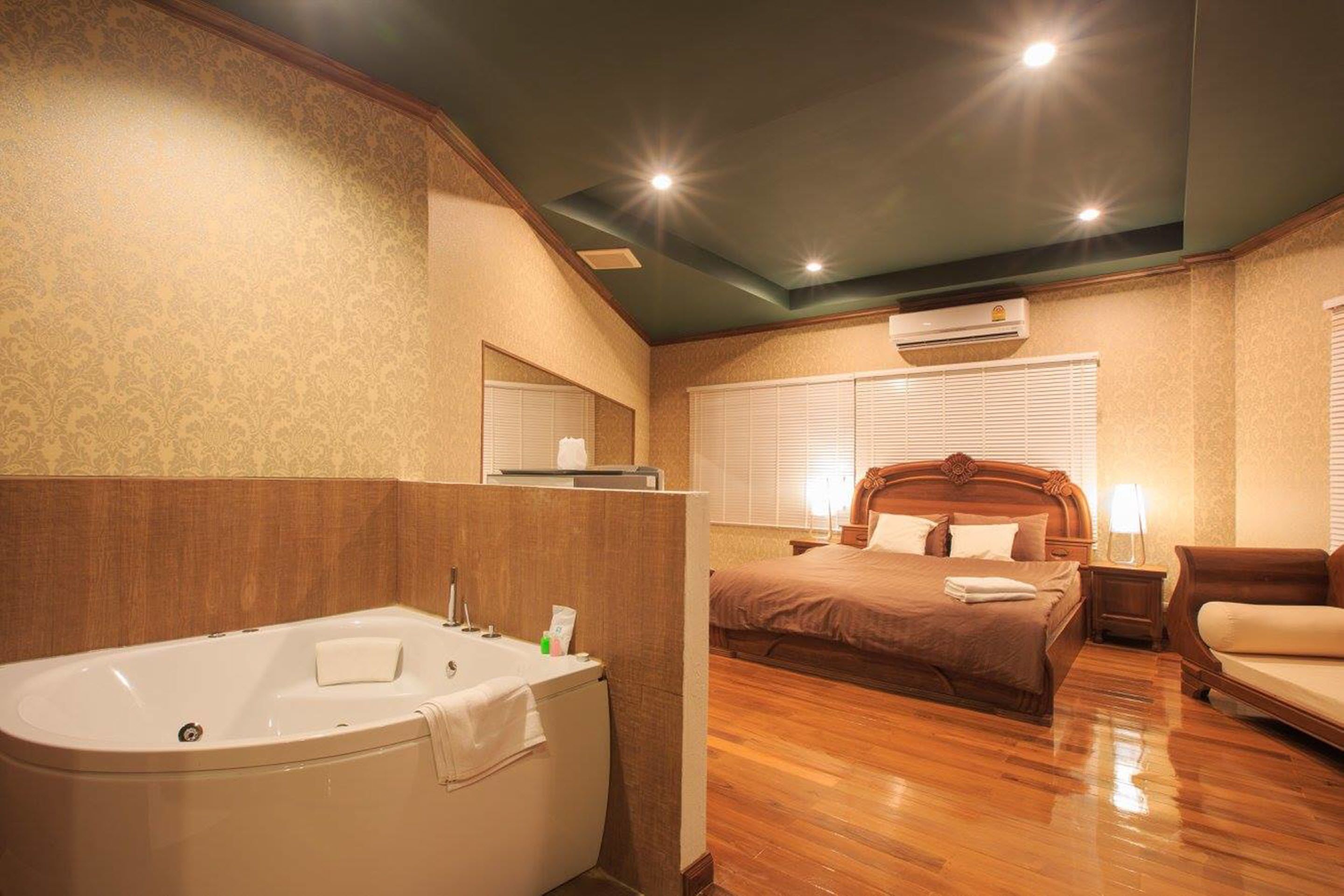 A spacious bedroom with a large bed, a separate sitting area, a bathtub, and a vanity with a mirror.