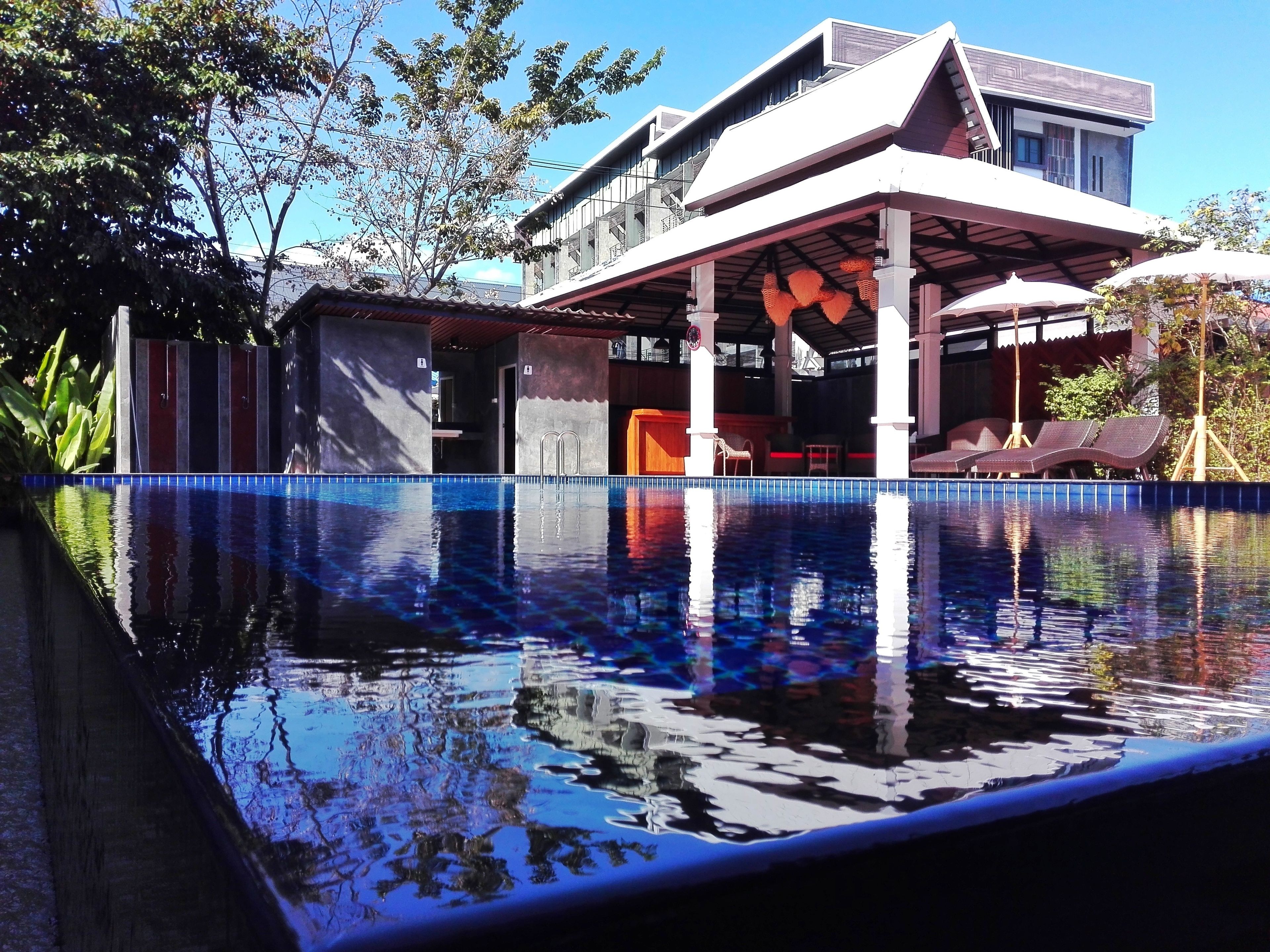 Un hotel moderno con piscina, mobiliario exterior y una zona cubierta con sombrillas.