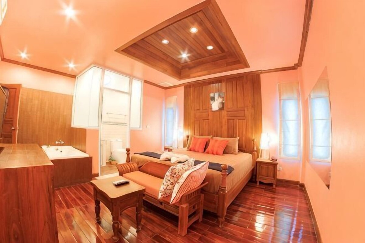 A bedroom with a wooden ceiling, a bed, a nightstand, a bedside table, a chair, and a window.