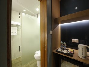 A modern bathroom with a glass partition, a white toilet, and a sink area with toiletries and a kettle.
