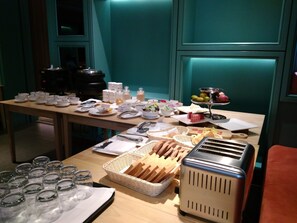 A breakfast buffet with various food items, a toaster, and glassware on a wooden table.