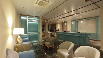 A modern lobby with a reception desk, seating area, and a staircase leading to upper floors.