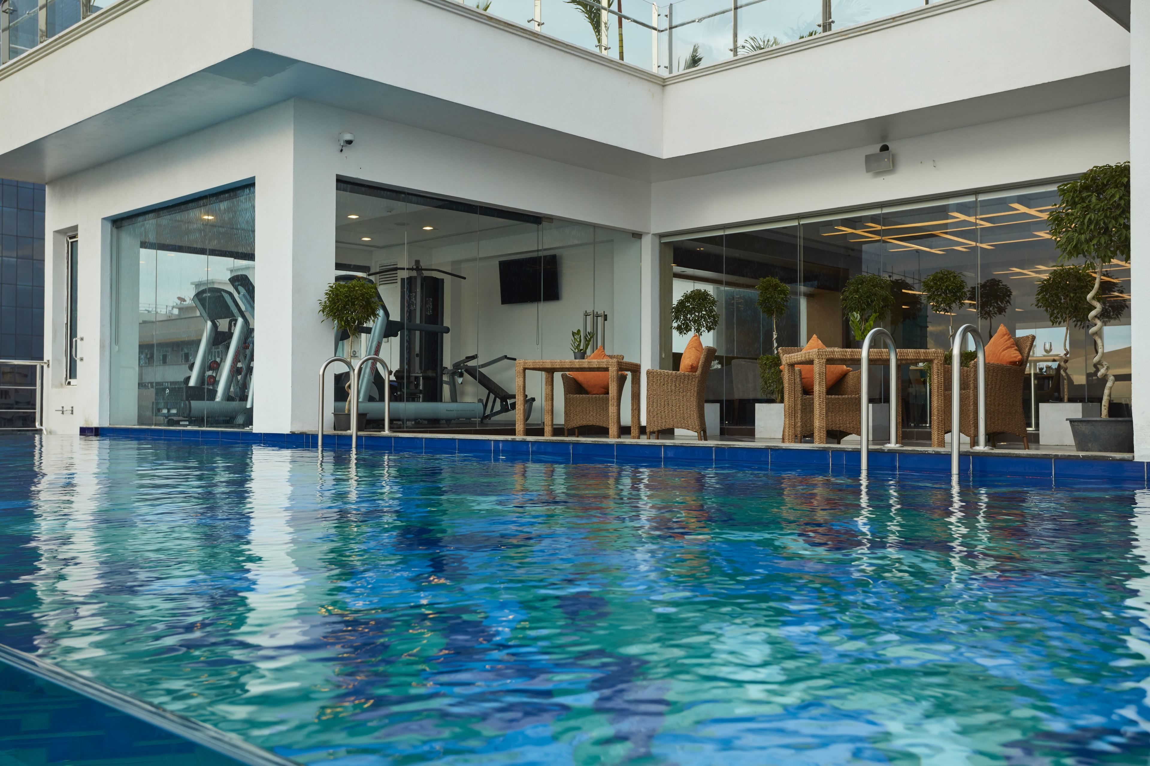 A modern indoor swimming pool with clear water, surrounded by wicker furniture and potted plants.