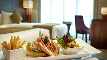 A breakfast tray with French fries, a sandwich, and a salad on a hotel room table.