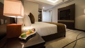 Una habitación de hotel moderna con una cama bien hecha, un televisor de pantalla plana montado en la pared y una mesita con fruta.