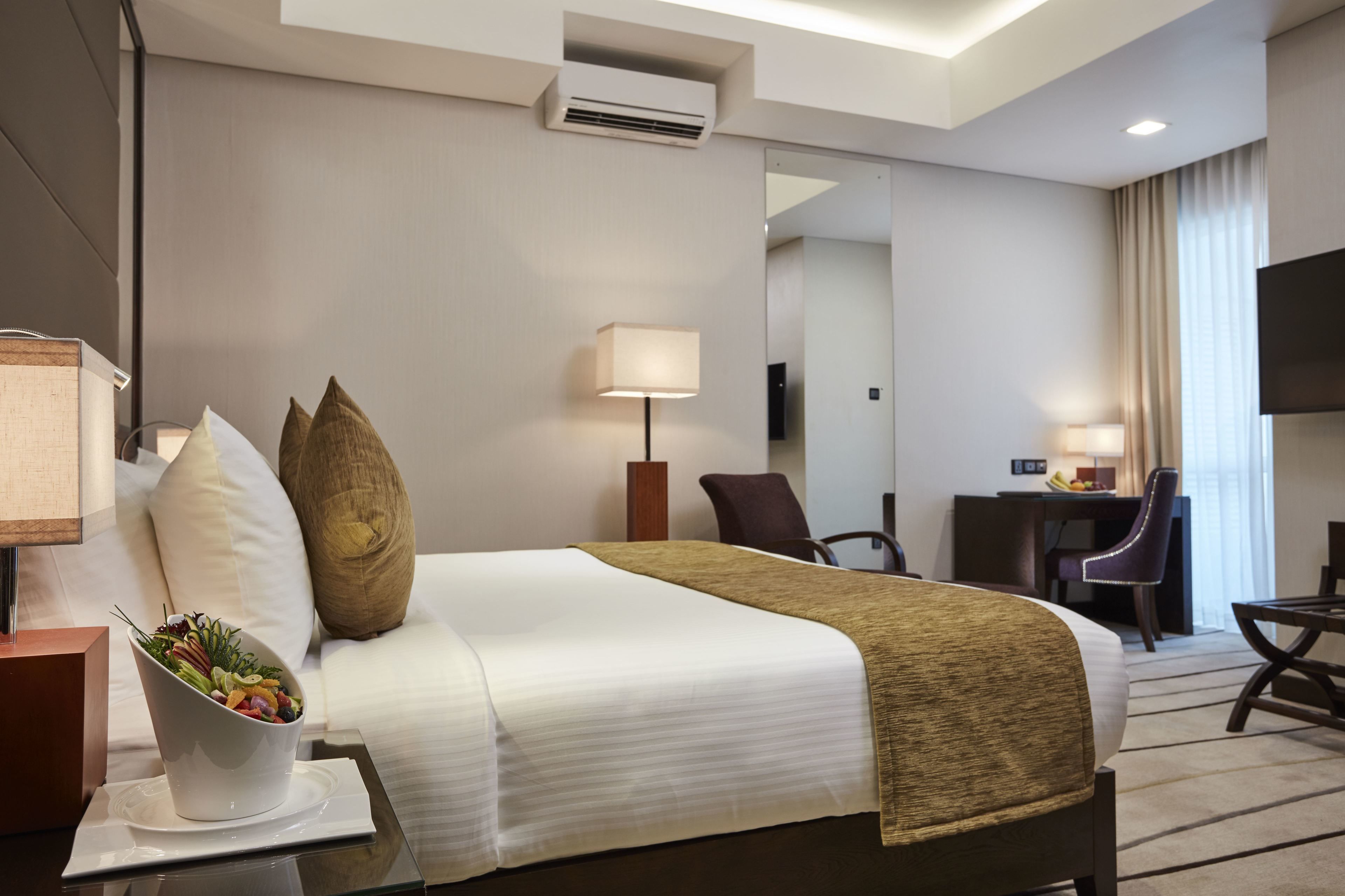 Habitación de hotel con una cama grande, un escritorio, una silla, una lámpara y una mesita con frutero.