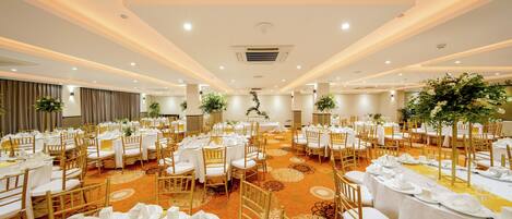 A banquet hall with round tables, white tablecloths, and gold chairs.
