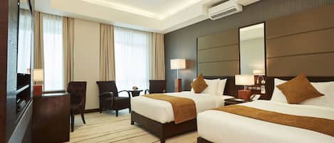 Quarto de hotel com duas camas, uma escrivaninha, uma cadeira, uma televisão e um aparelho de ar condicionado.