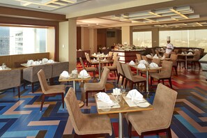 A modern restaurant with booths and tables, a chef in uniform, and a city view.