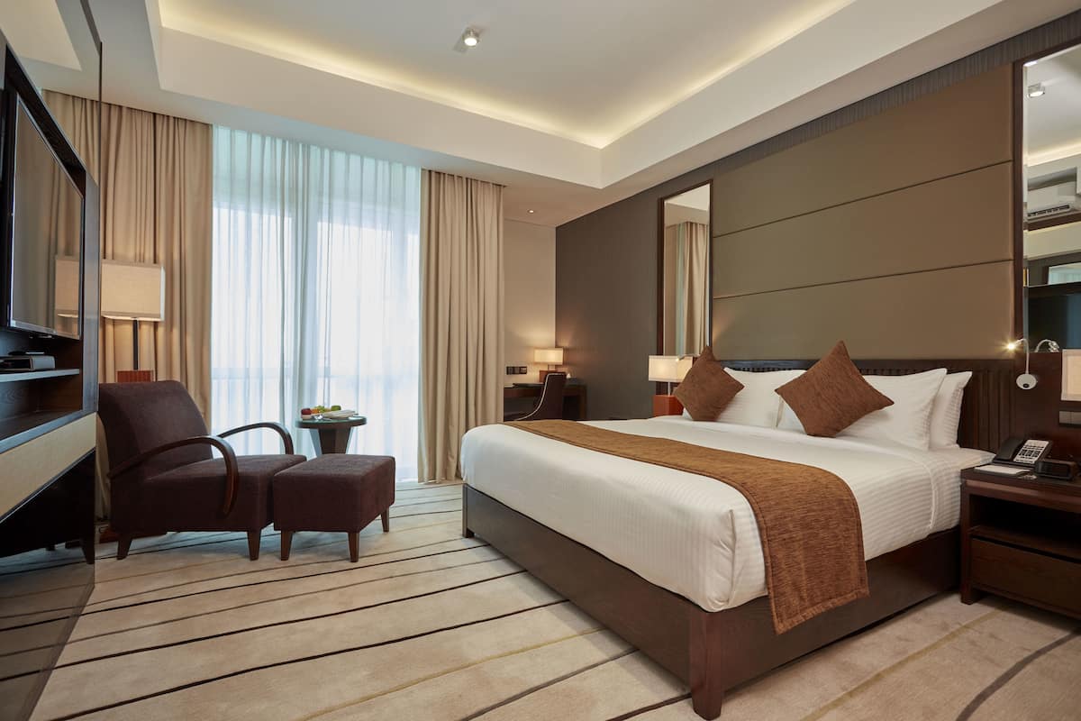 A hotel room with a large bed, a desk, a chair, a TV, and a large window with curtains.
