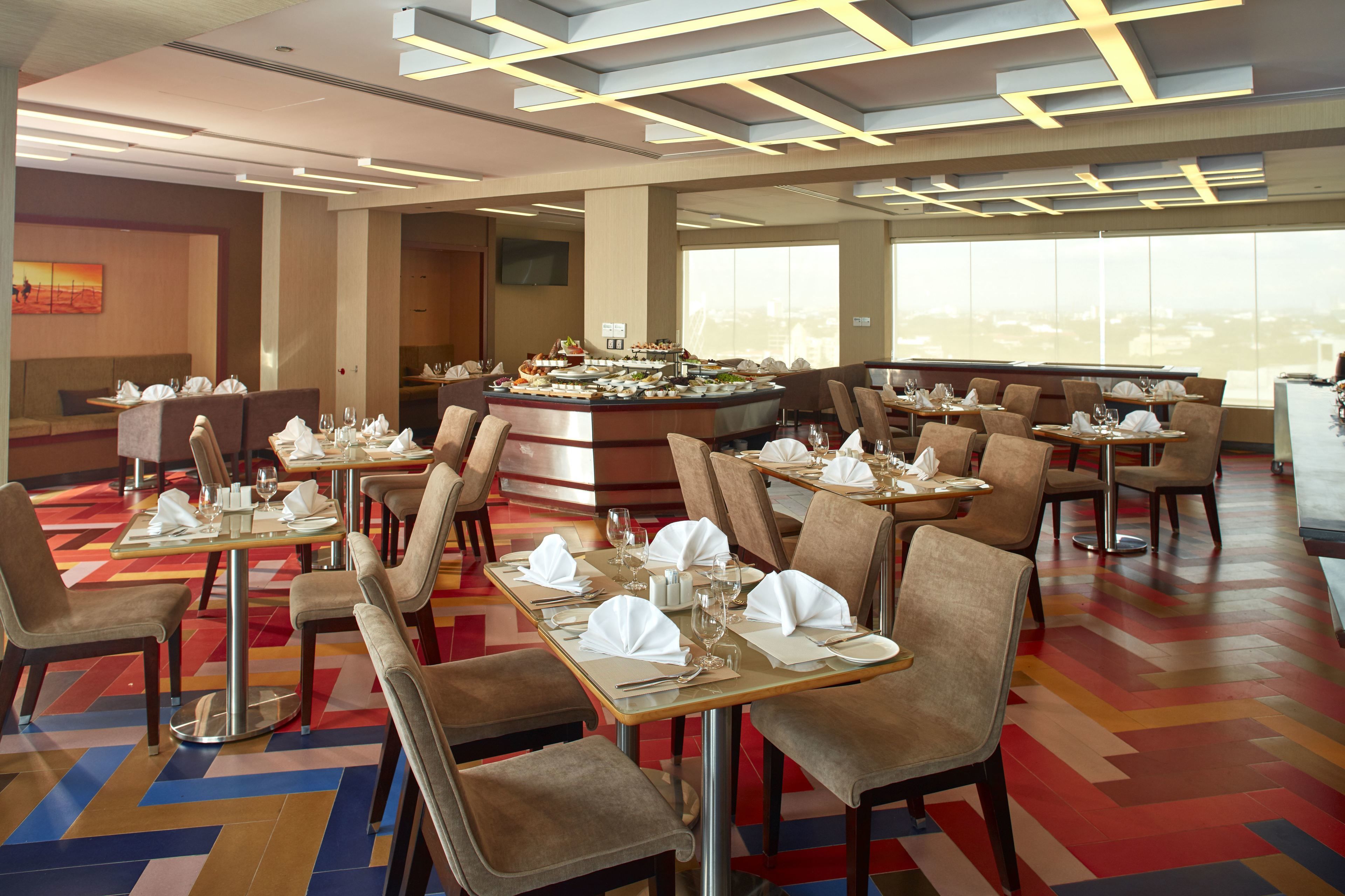 A modern restaurant with a central bar, high ceilings, and a colorful floor pattern.