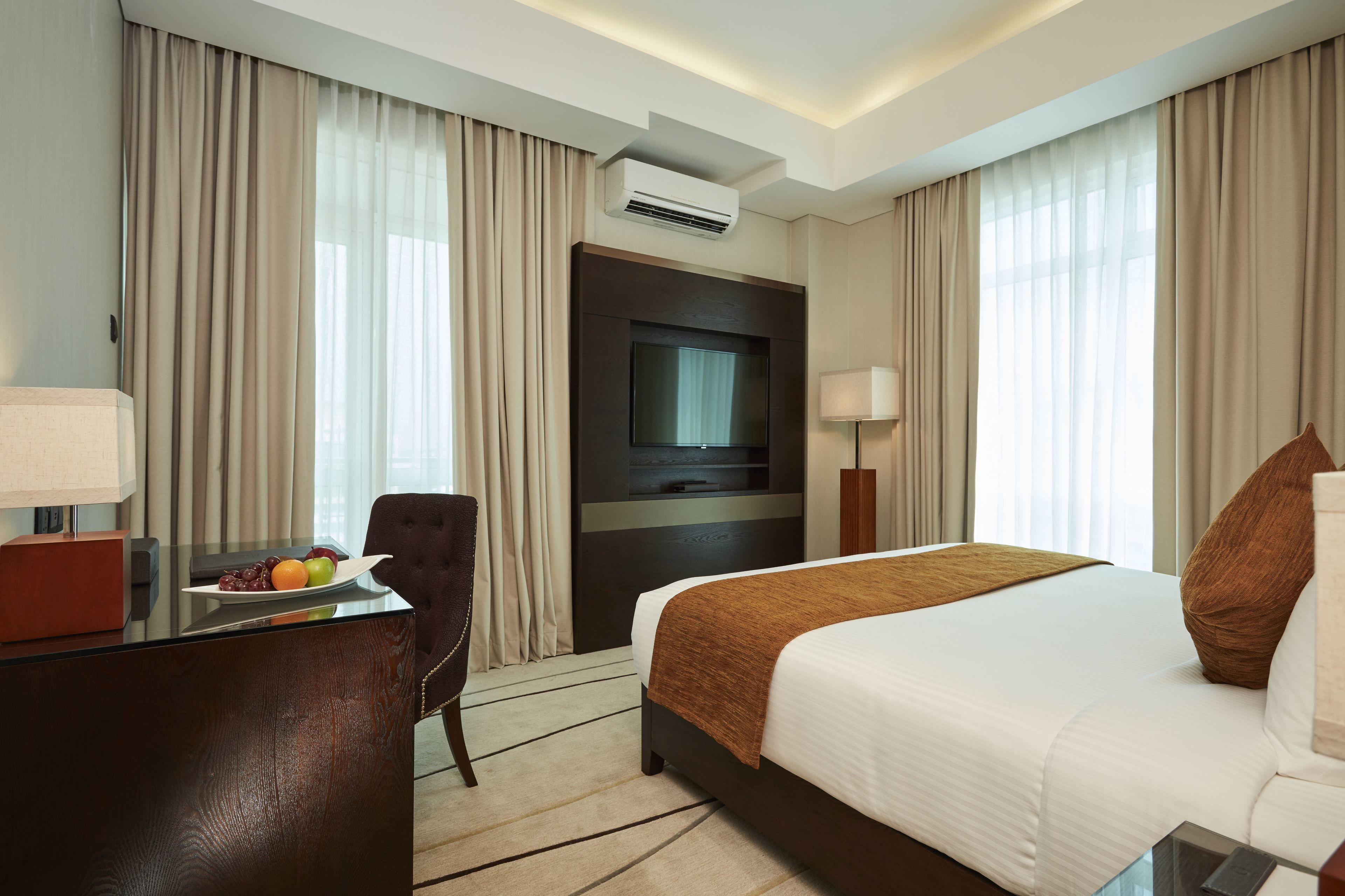 A hotel room with a bed, a desk with a laptop, a TV, and a fruit plate.