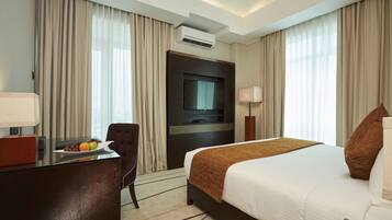 A hotel room with a bed, a desk with a laptop, a TV, and a fruit plate.