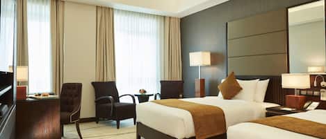 A hotel room with two beds, a desk, a chair, a TV, and a large mirror.