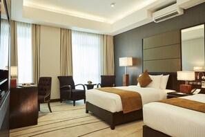 A hotel room with two beds, a desk, a chair, a TV, and a large mirror.