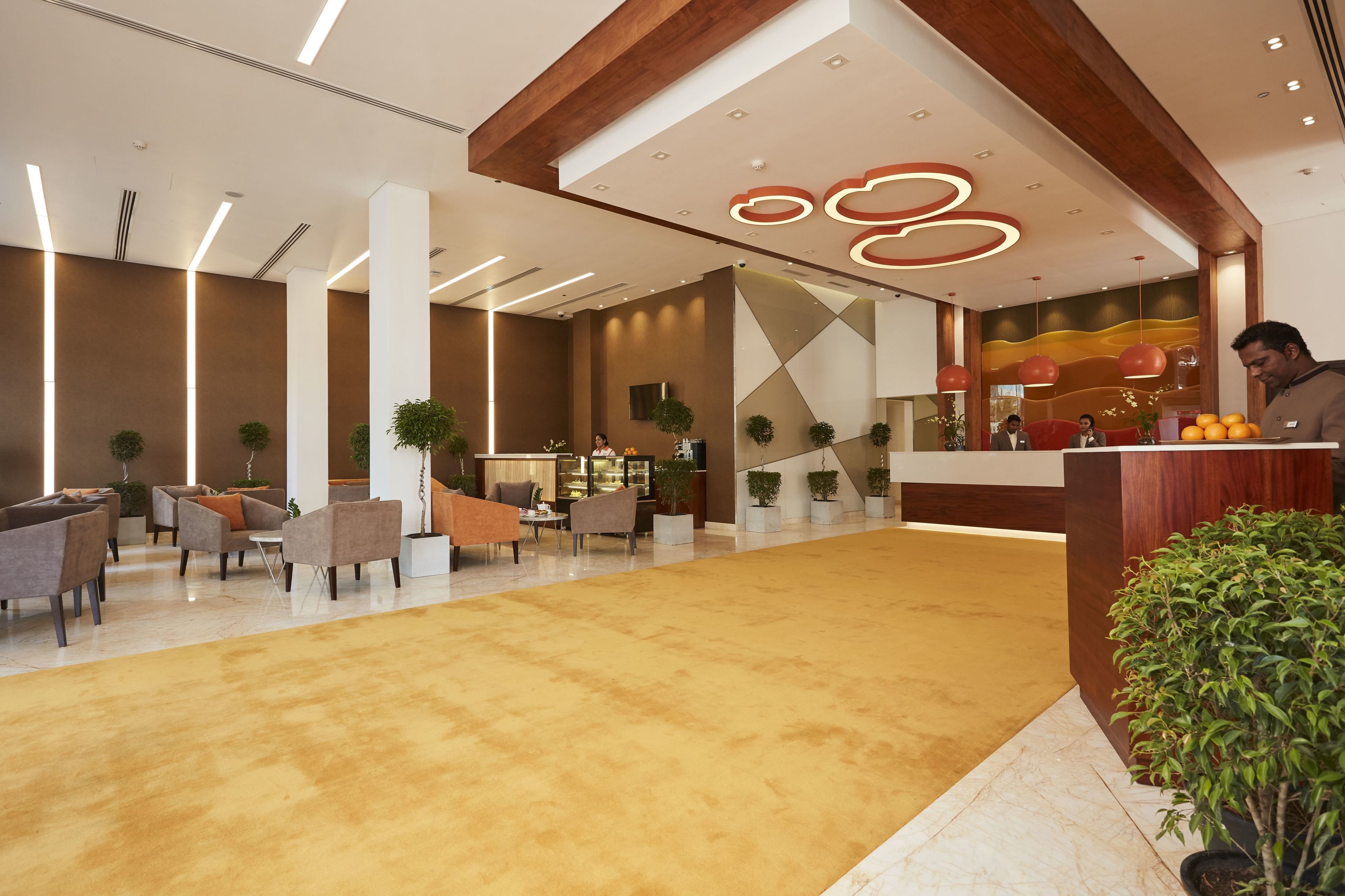 A modern hotel lobby with a reception desk, seating area, and decorative plants.