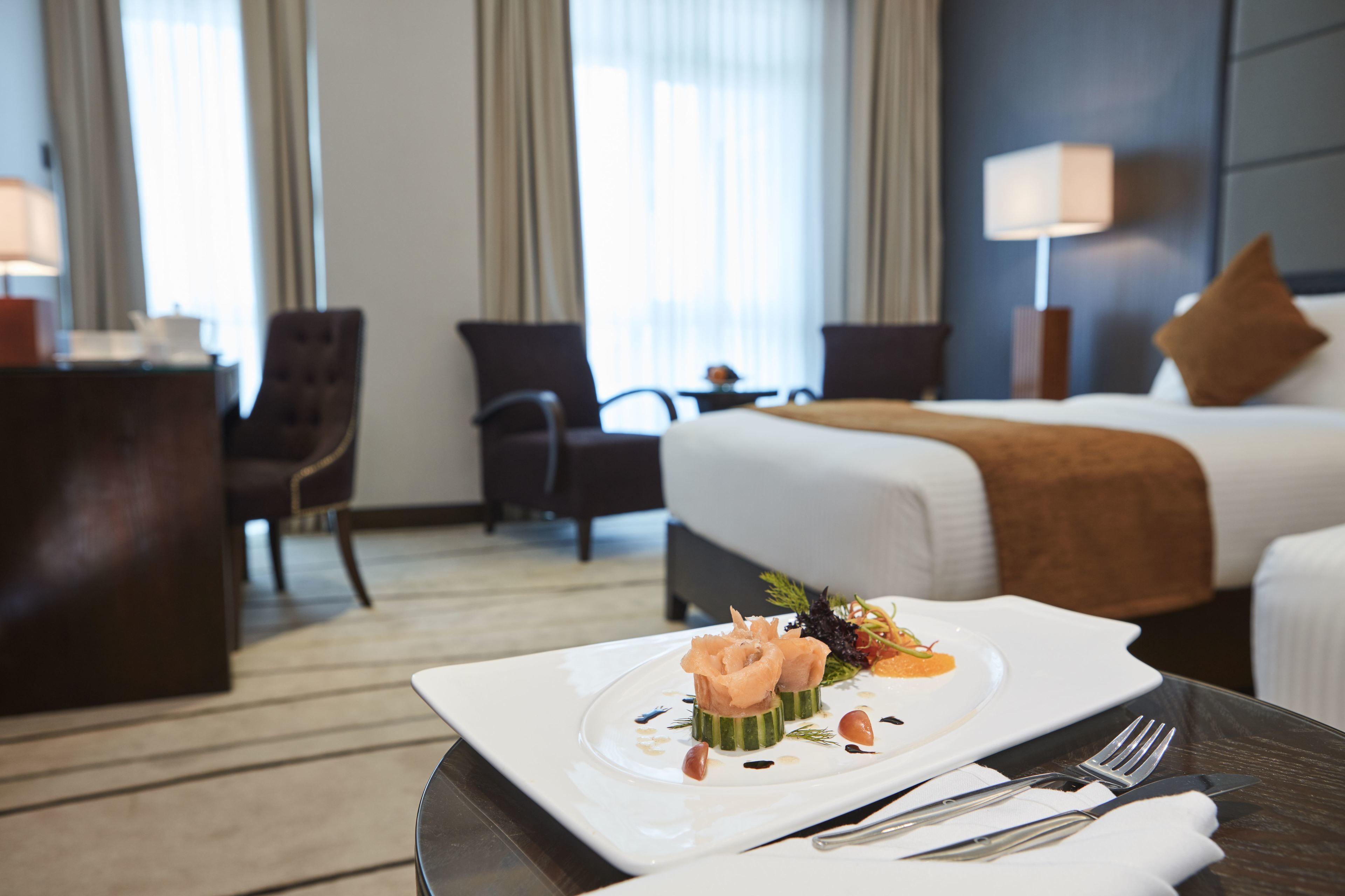 A hotel room with a neatly made bed, a dining table with a plate of food, and a chair.