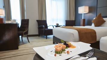 A hotel room with a neatly made bed, a dining table with a plate of food, and a chair.