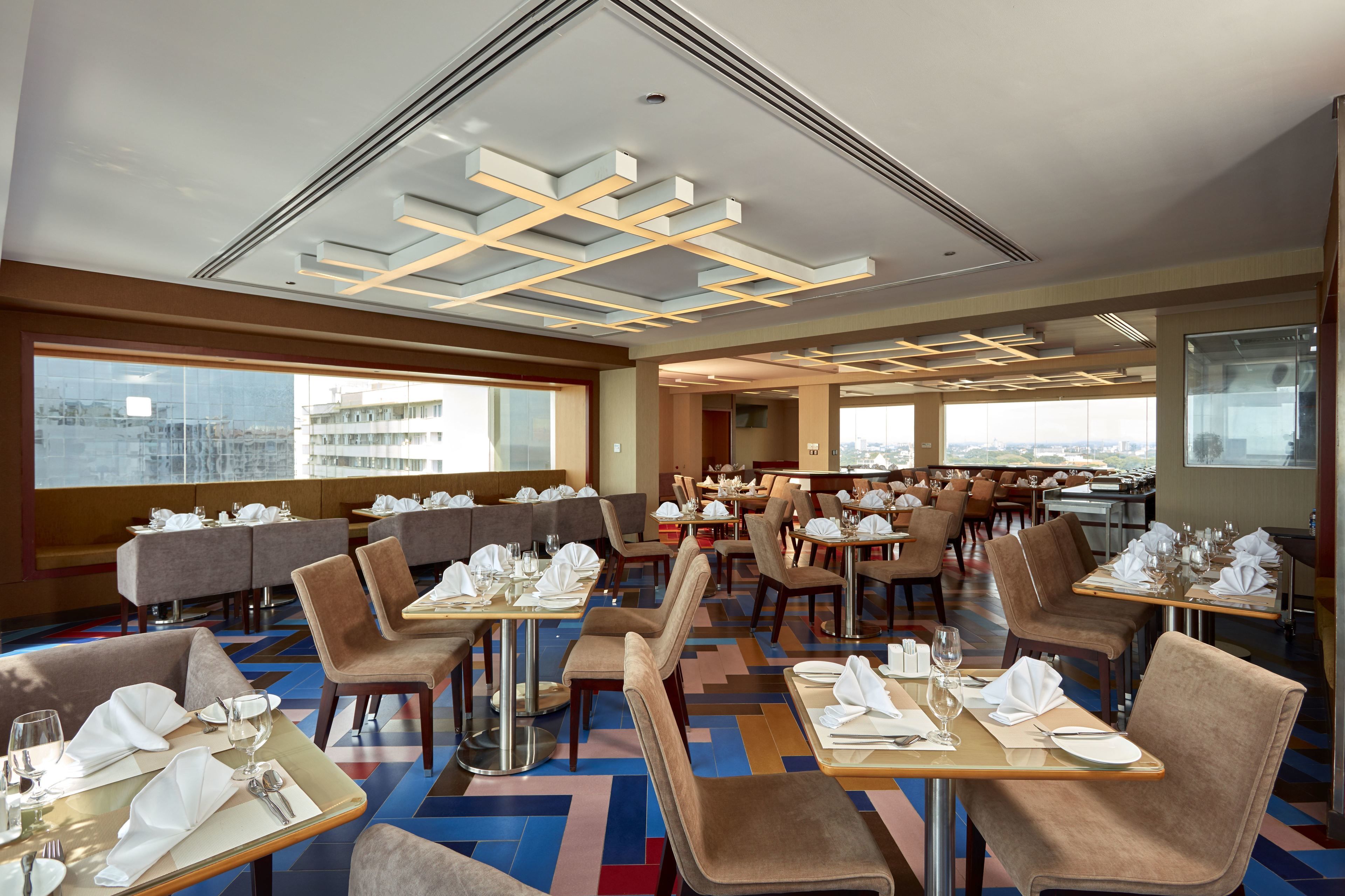 Ein modernes Restaurant mit hohen Tischen und Sitzgelegenheiten, großen Fenstern mit Blick auf die Stadt und einem zeitgemäßen Deckenstil.