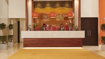 Zona de recepción de hotel con diseño moderno, que incluye un mostrador de madera, una alfombra amarilla grande y un techo con luminarias circulares.