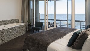Ein modernes Schlafzimmer mit einem großen Bett, einer Badewanne und Meerblick durch eine offene Tür.