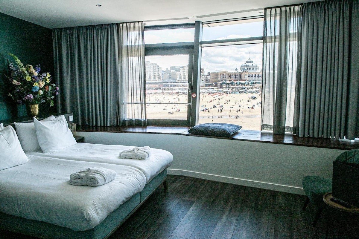 A hotel room with a large bed, a view of a beach, and a cityscape.